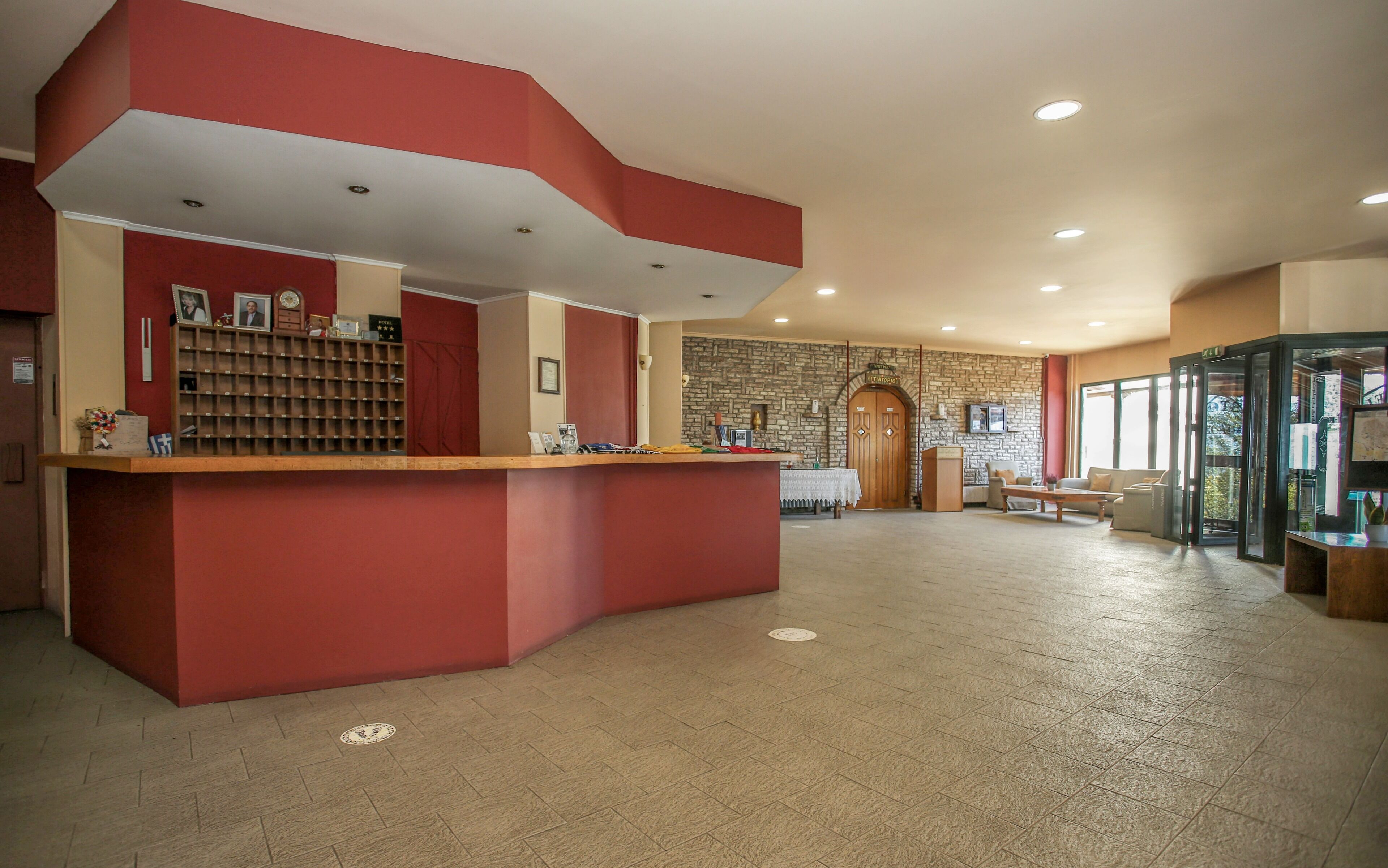 A hotel reception area with a red counter, a stone wall, and a wooden door.