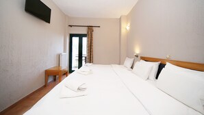 A hotel room with a large bed, a wooden bench, a TV mounted on the wall, and a door leading to a balcony. - Lecadin Hotel (Karpenisi)