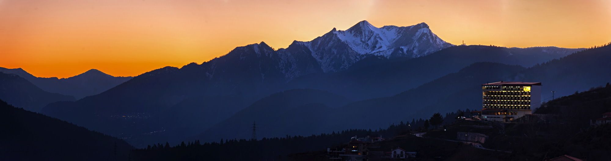 A hotel with a modern design, located in a mountainous area with a view of snow-capped peaks.