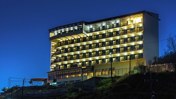 A multi-story hotel with a curved facade, illuminated balconies, and a prominent entrance at the base. - Lecadin Hotel (Karpenisi)
