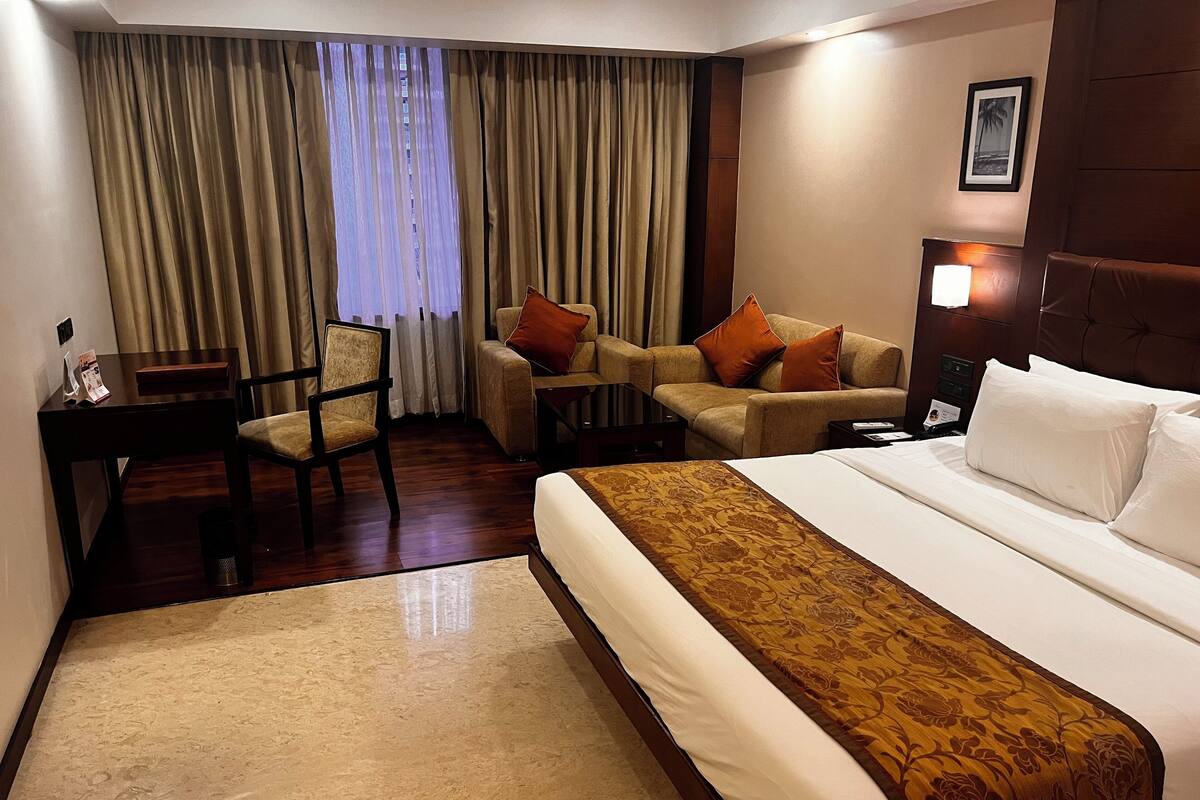 A hotel room with a large bed, a sofa, a chair, a small table, and a desk.