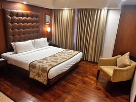 Una habitación de hotel con una cama grande, cabecera de madera, mesita de noche con lámpara y una silla.