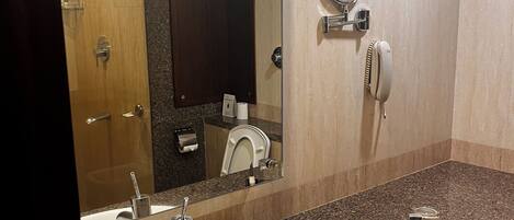 A bathroom with a white sink, a mirror, a towel dispenser, and a toilet.
