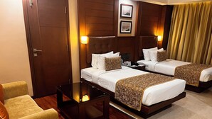 A hotel room with two beds, a small table, a chair, wooden flooring, and wall-mounted lamps. - The Ocean Pearl (Mangaluru)