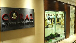 A sign for 'CORAL Multi Cuisine Fine Dining Restaurant' with a glass window reflecting the interior dining area. - The Ocean Pearl (Mangaluru)