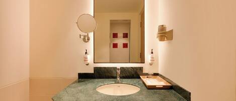 A bathroom with a marble sink, a mirror, and a towel dispenser.