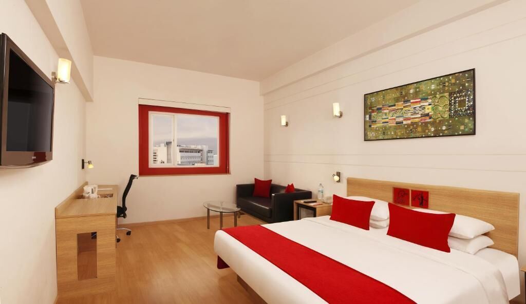 Hotelkamer met een bed, bureau, stoel, televisie, raam met uitzicht op de stad en een schilderij aan de muur.