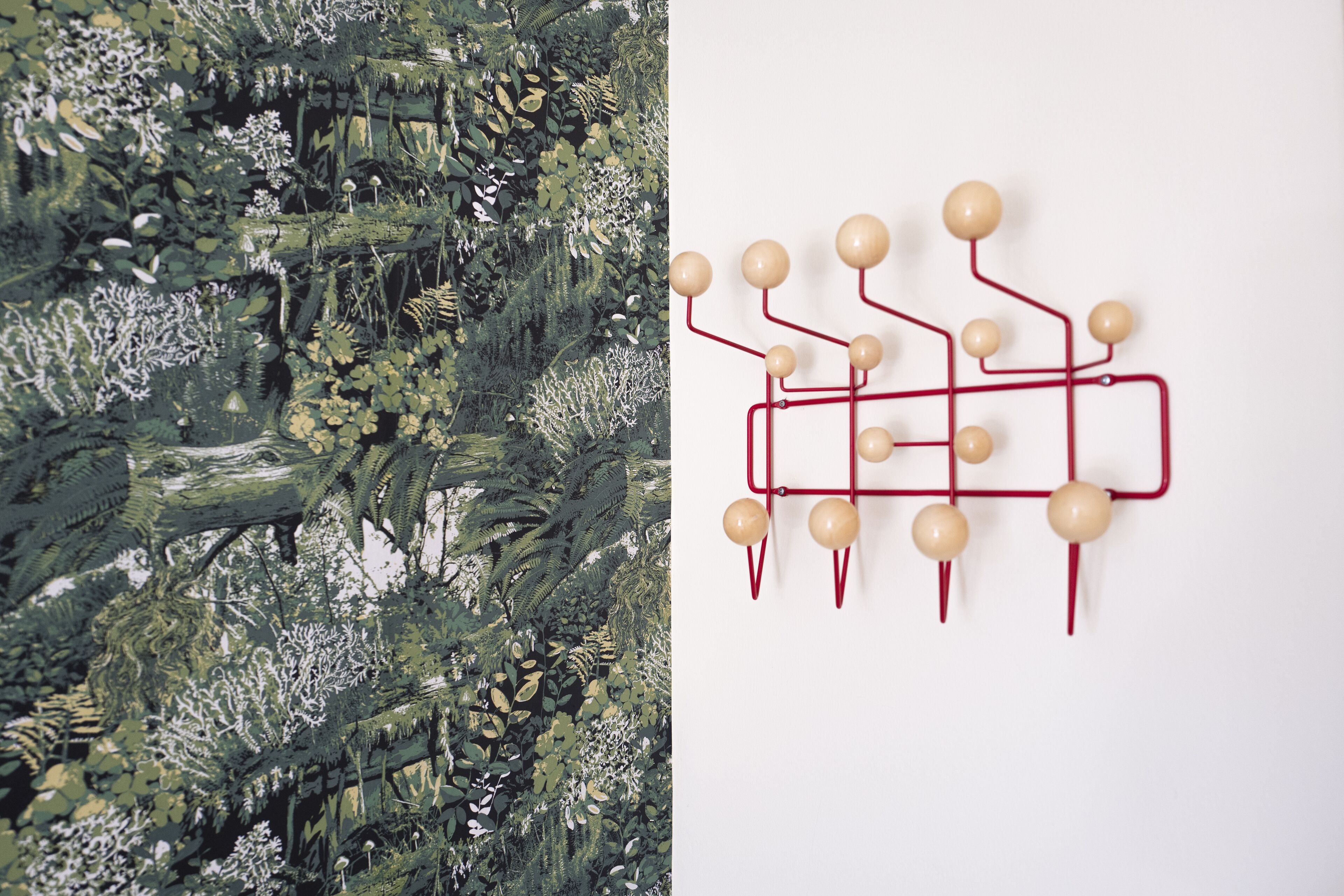 A wall with a red abstract art installation and a dense green foliage wall.
