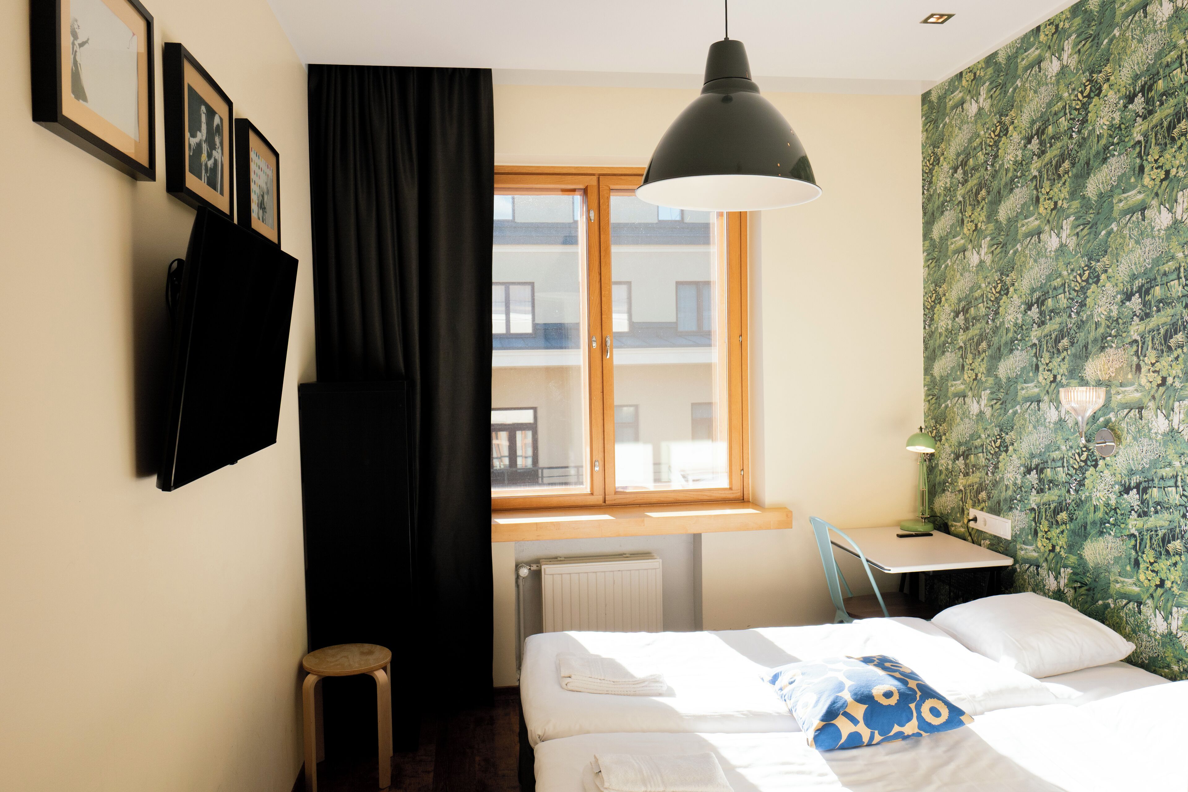 A hotel room with a bed, a desk, a chair, a window, and a radiator.
