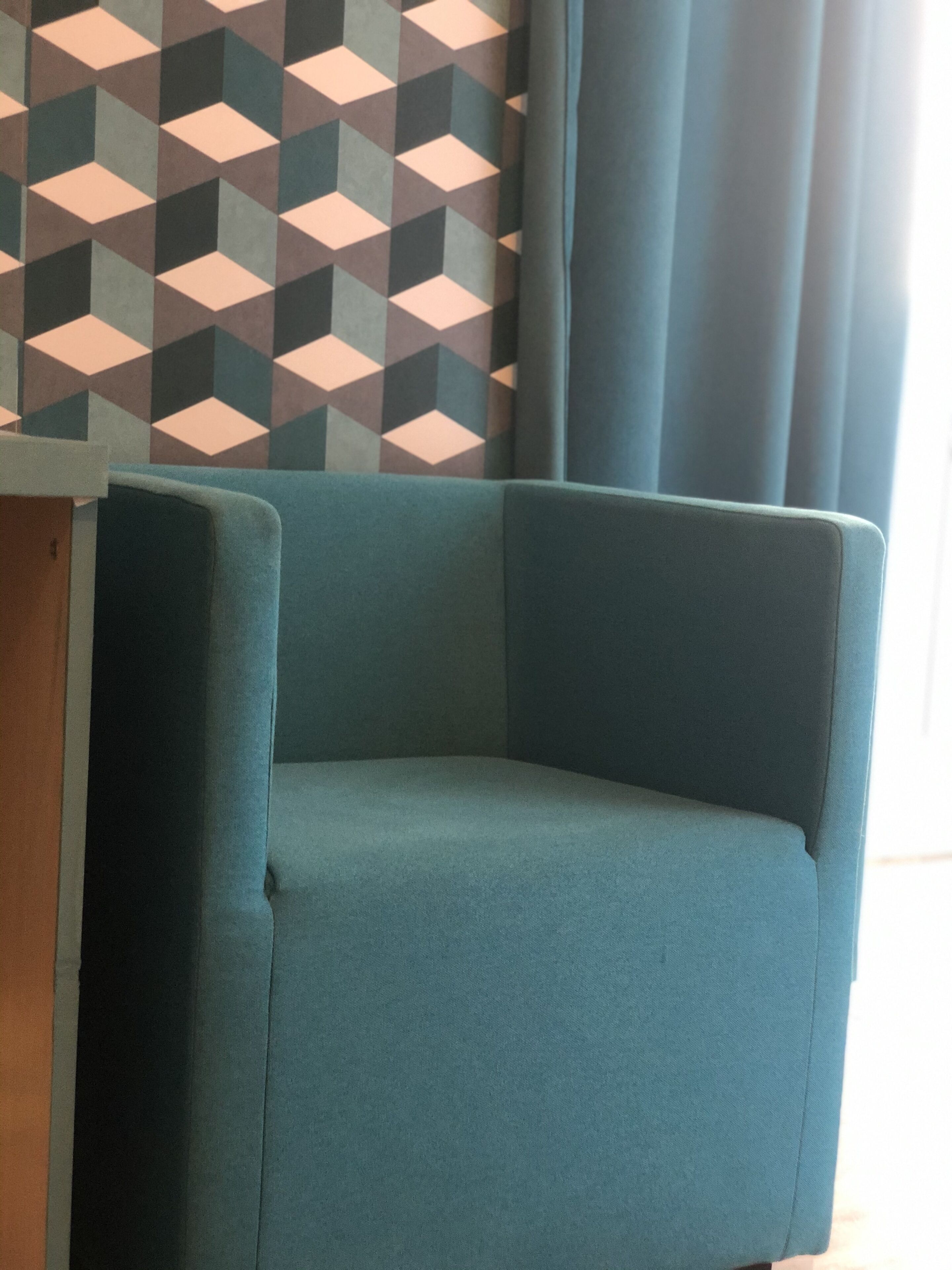 Un sillón de esquina tapizado en tela color turquesa, ubicado frente a una pared con papel tapiz de estampado geométrico.