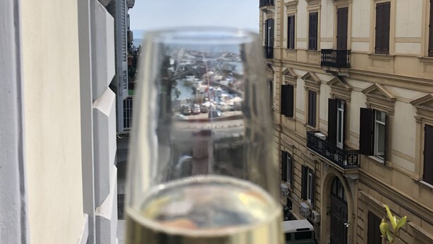A glass of white wine held in front of a balcony overlooking a cityscape with historic buildings and a clear sky. - H Rooms Boutique Hotel (Naples)