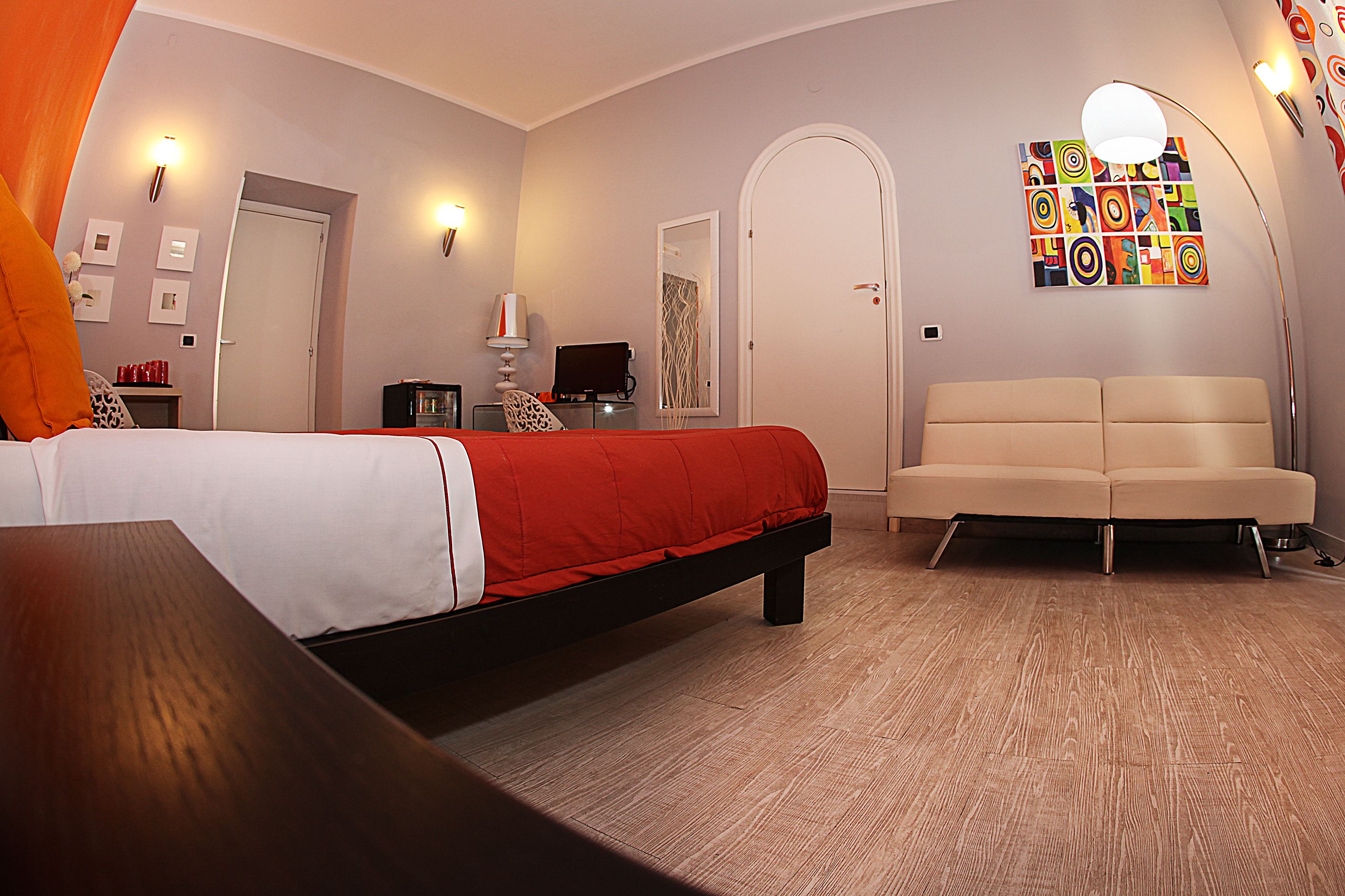 A modern hotel room with a bed, a sofa, a desk, and a TV.
