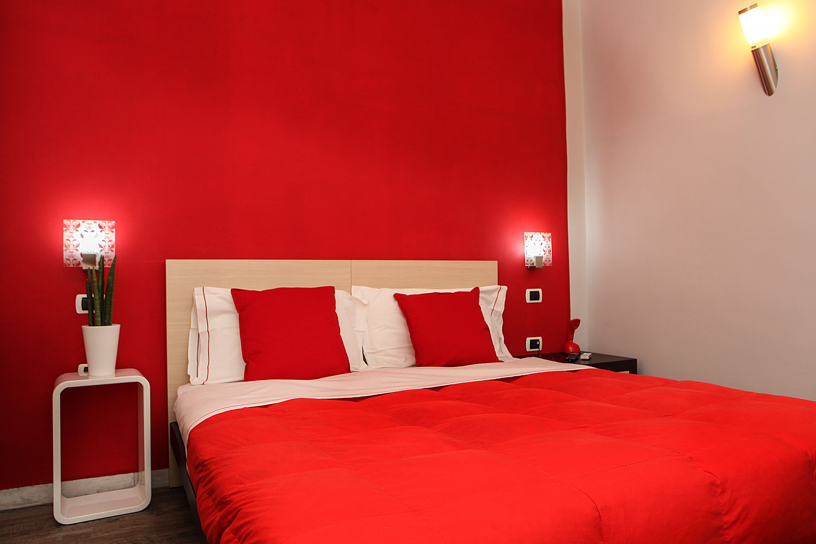 Habitación de hotel con una pared roja, cabecera de madera, colcha roja y dos mesitas de noche con lámparas rojas.