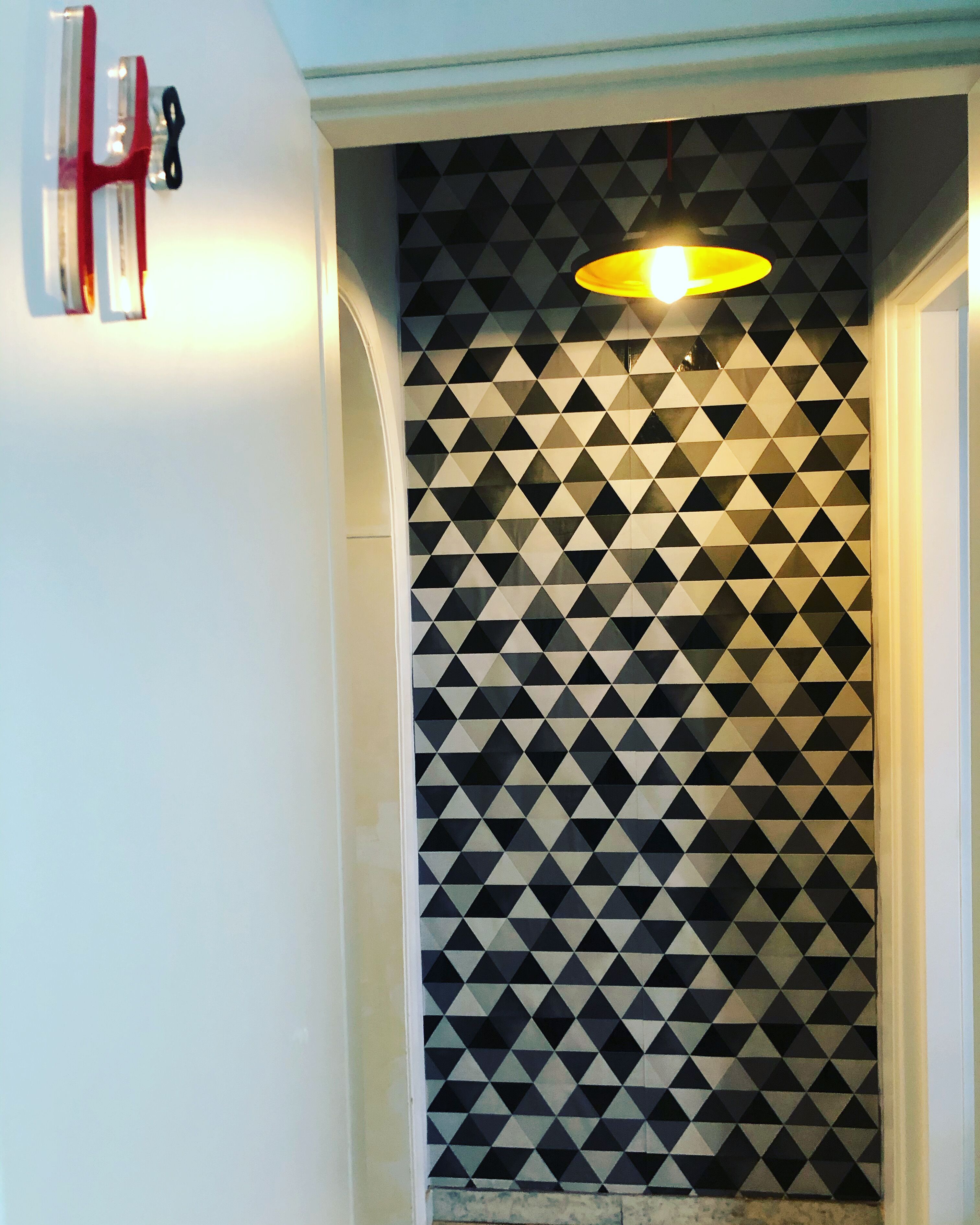 A hallway with a geometric patterned wall, a light fixture, and a fire alarm on the wall.