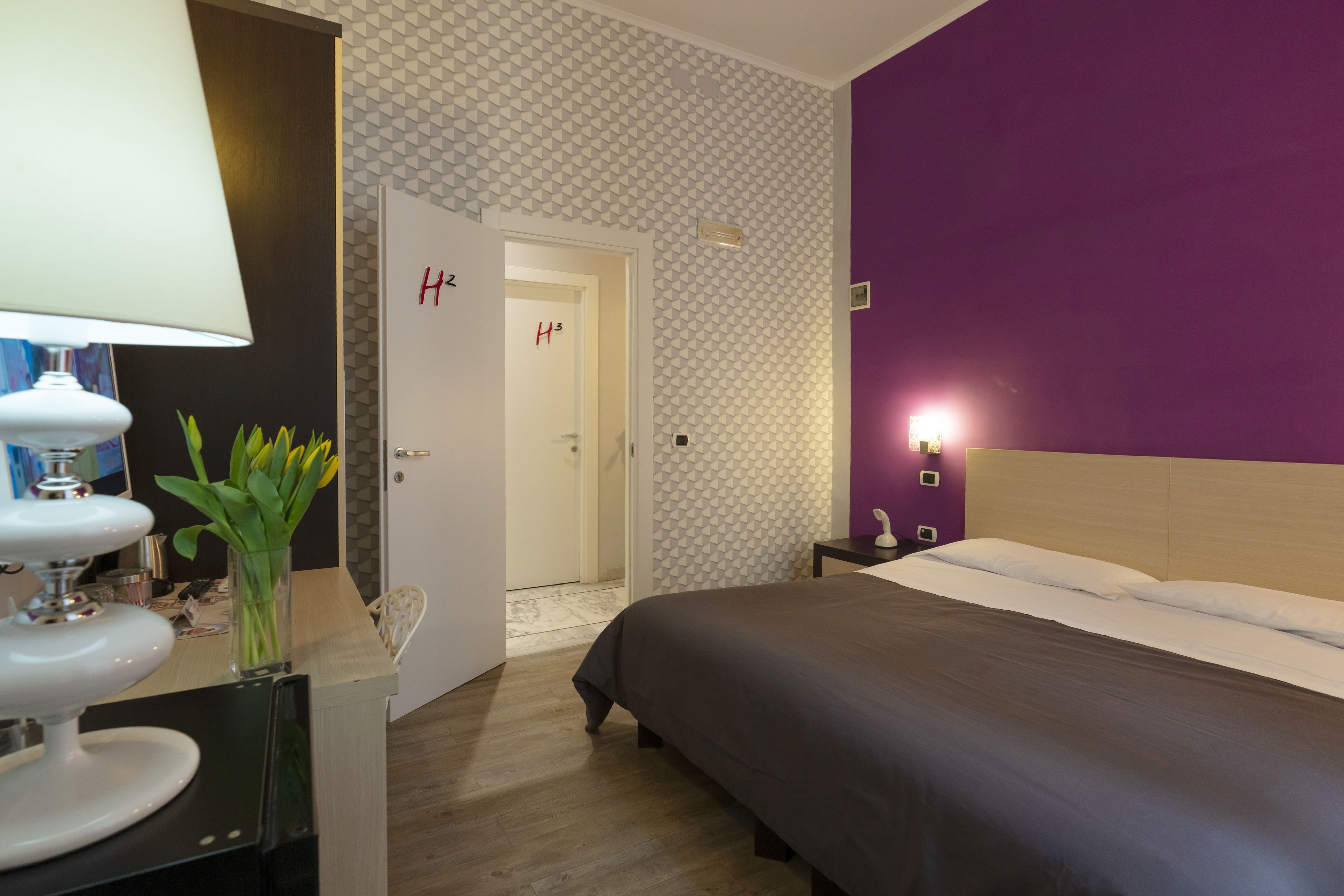 A hotel room with a bed, a nightstand, a lamp, and a vase with flowers.