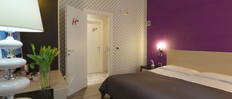 A hotel room with a bed, a nightstand, a lamp, and a vase with flowers.