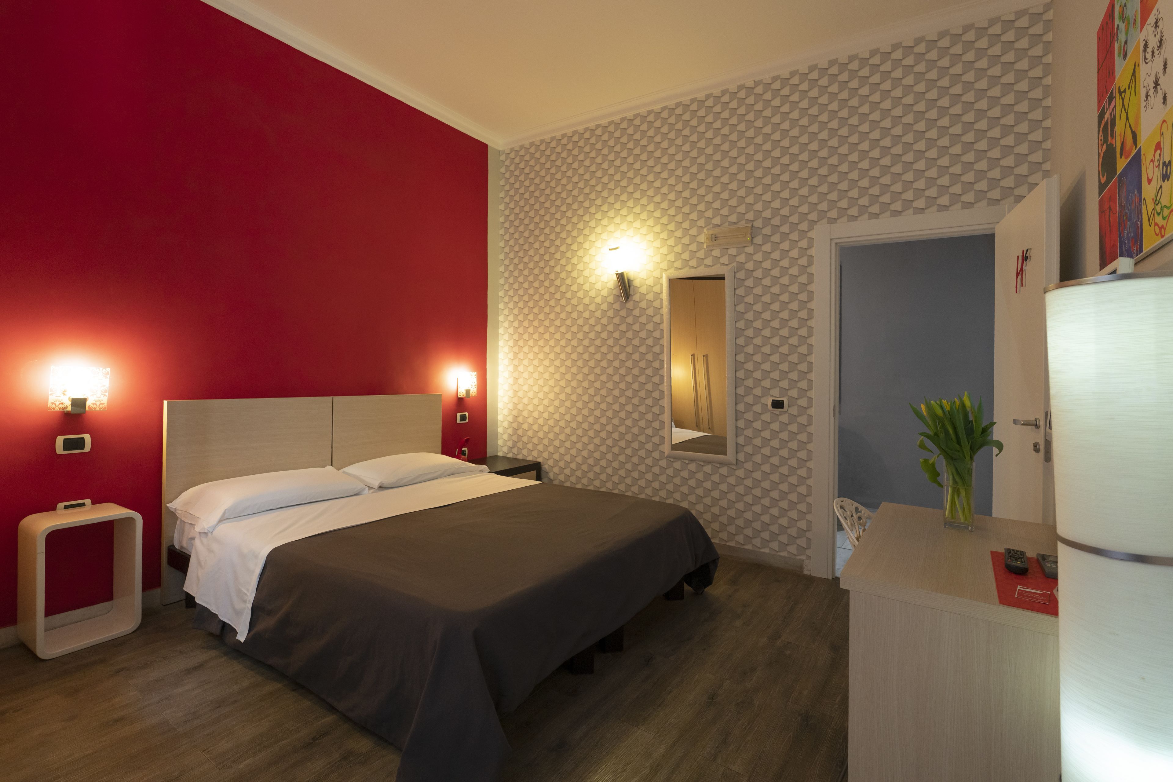 A hotel room with a bed, bedside tables, a mirror, a dresser, and a door.