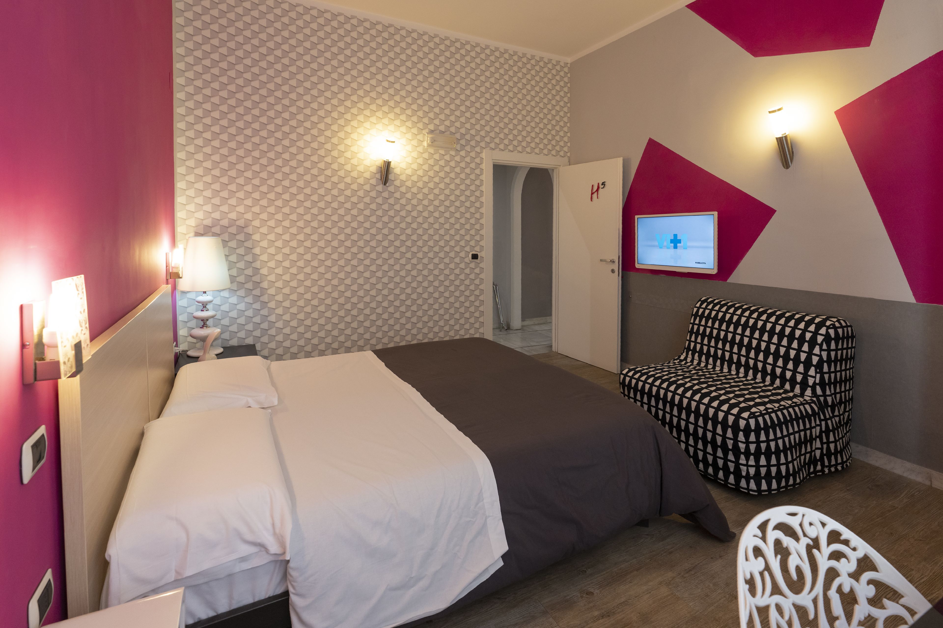 Una habitación de hotel con una cama, una silla y un televisor en la pared.