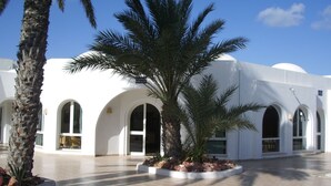 A white building with arched windows and a palm tree in the center. - Menzel Dija (Djerba Midun)
