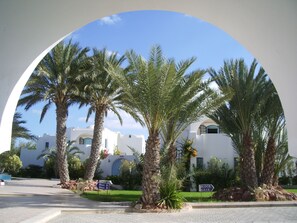 A view through an archway of a building with palm trees in the foreground and a clear blue sky. - Menzel Dija (Djerba Midun)