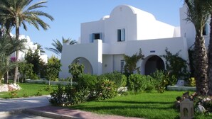 A white building with arched windows and a curved roof, surrounded by greenery and palm trees. - Menzel Dija (Djerba Midun)