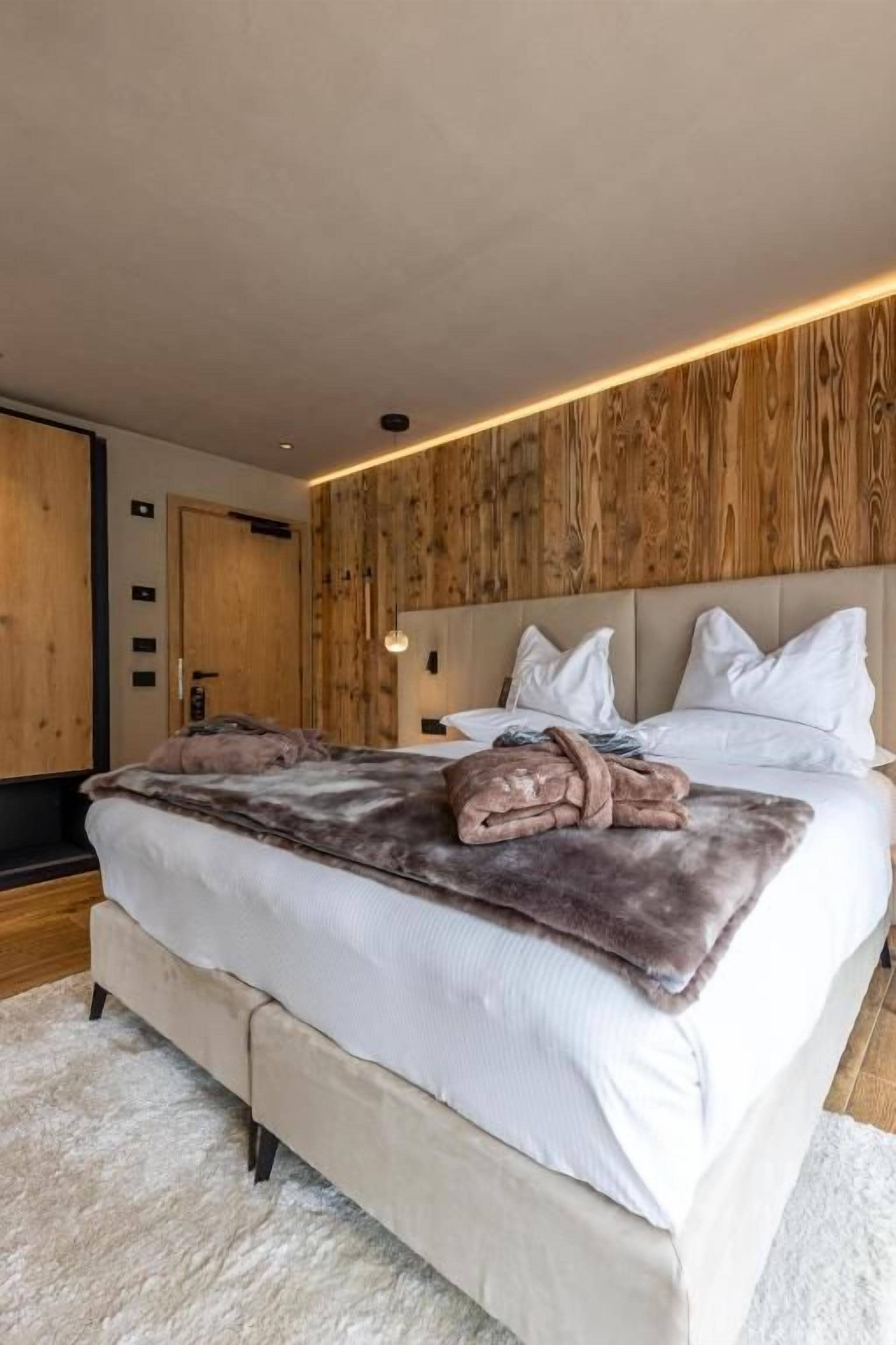 A bedroom with a large bed, wooden paneling on the wall, and a modern light fixture.
