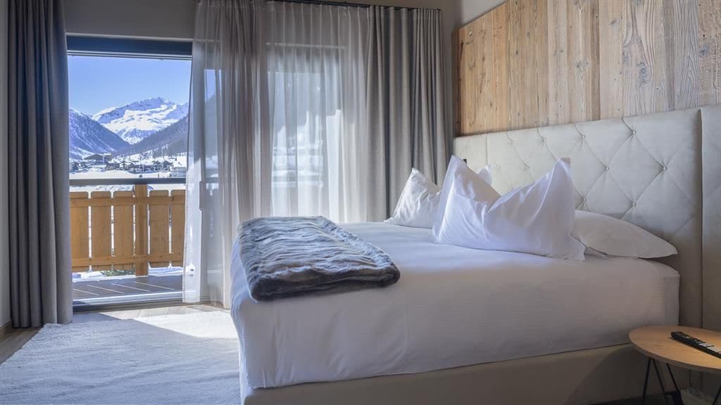Ein Hotelzimmer mit Bett, Bergblick und einem Balkon mit Holzwertlauf.