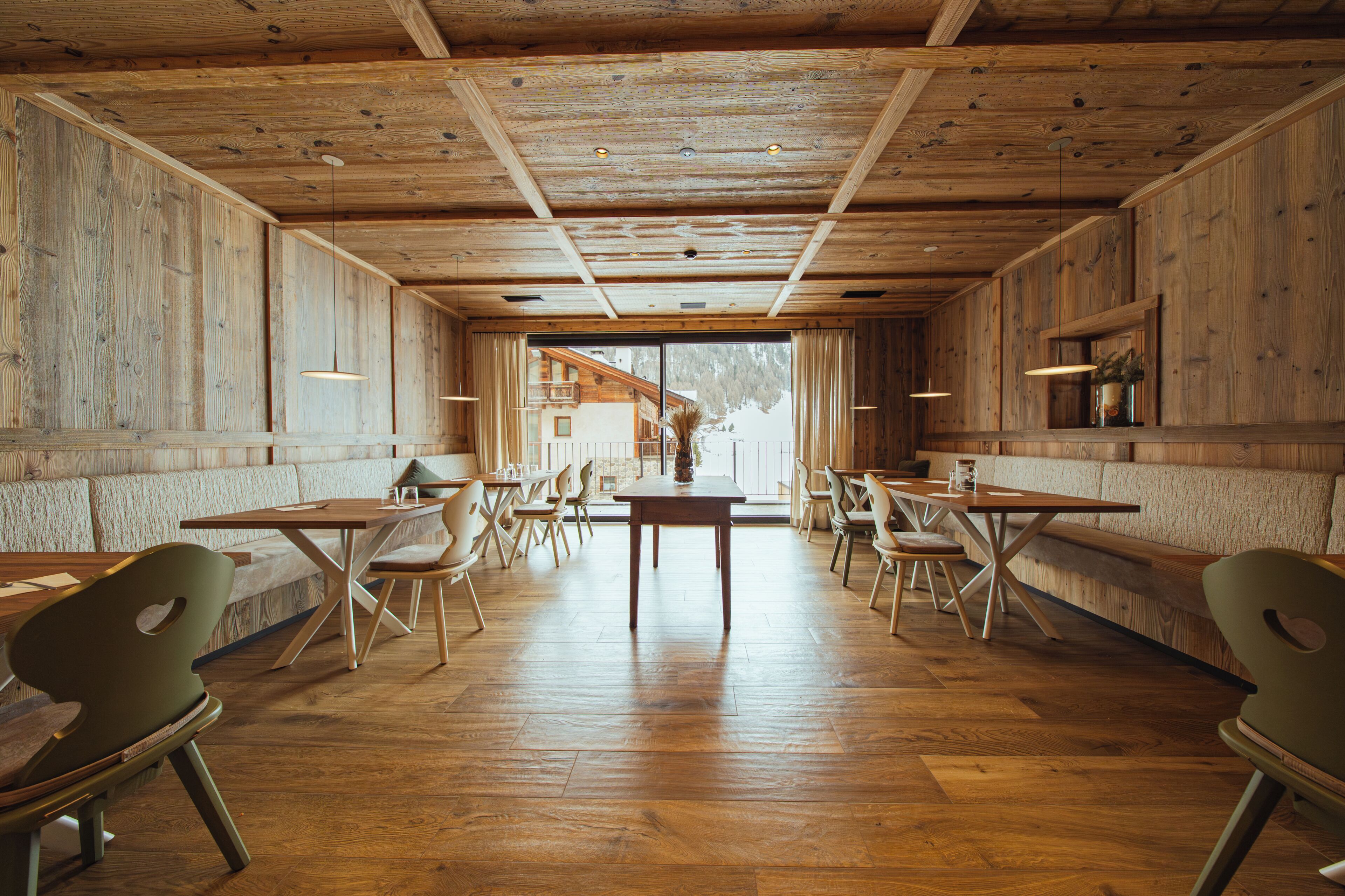 A restaurant with wooden walls and ceiling, wooden tables and chairs, and a view through a large window.