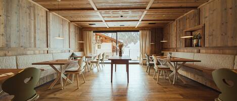 A restaurant with wooden walls and ceiling, wooden tables and chairs, and a view through a large window.