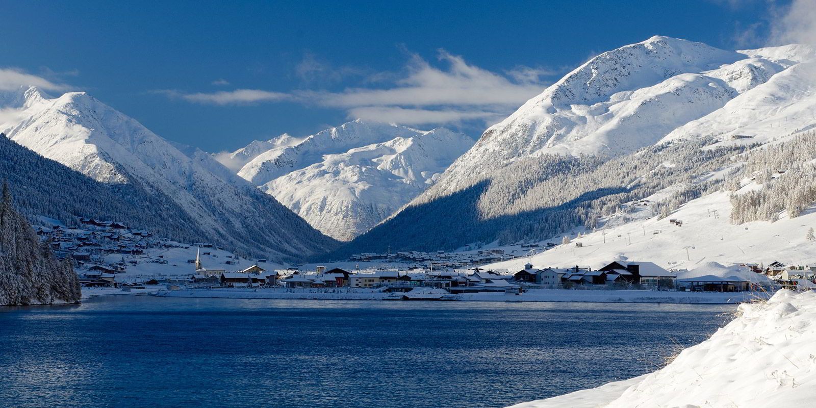 A snow-covered mountain landscape with a small village by a lake.
