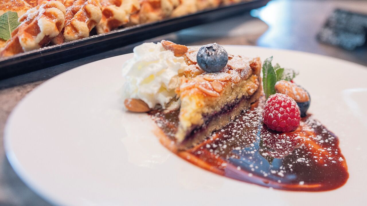 A dessert plate with a slice of pie topped with whipped cream, blueberries, raspberries, and almonds, accompanied by a berry sauce.