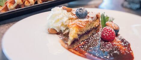 A dessert plate with a slice of pie topped with whipped cream, blueberries, raspberries, and almonds, accompanied by a berry sauce.