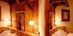 A wooden cabin-style room with a large mirror, two bedside lamps, and a window with curtains.
