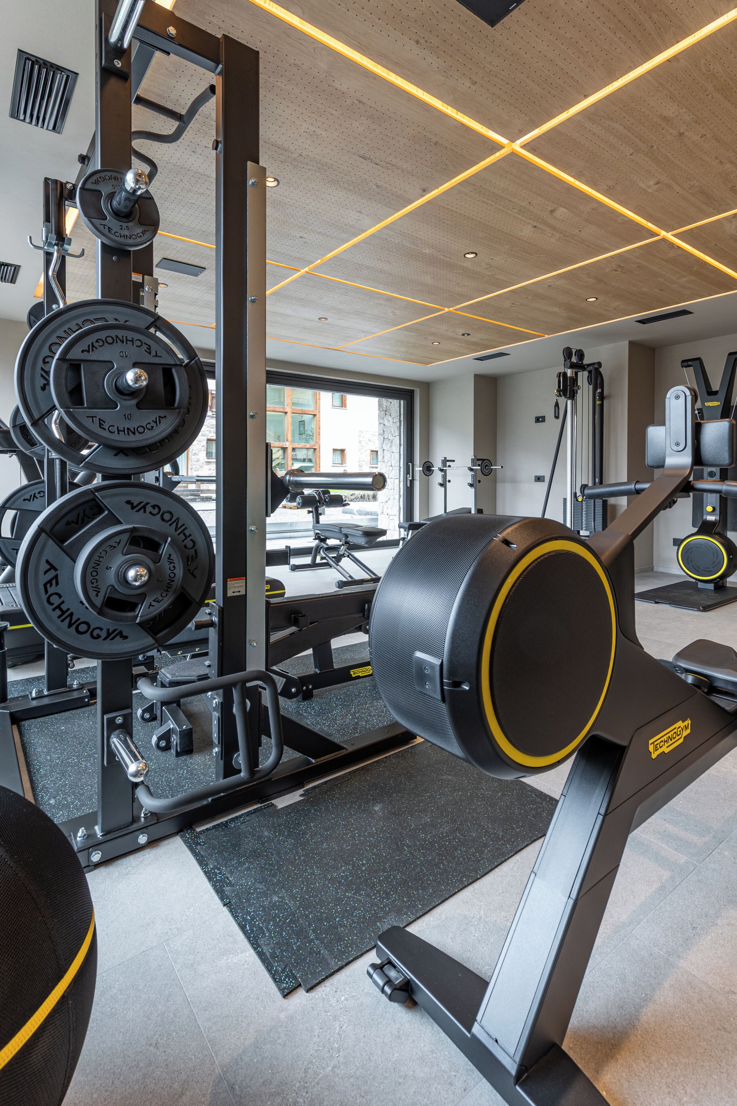A gym with weightlifting equipment, a treadmill, and a window with a view of buildings.