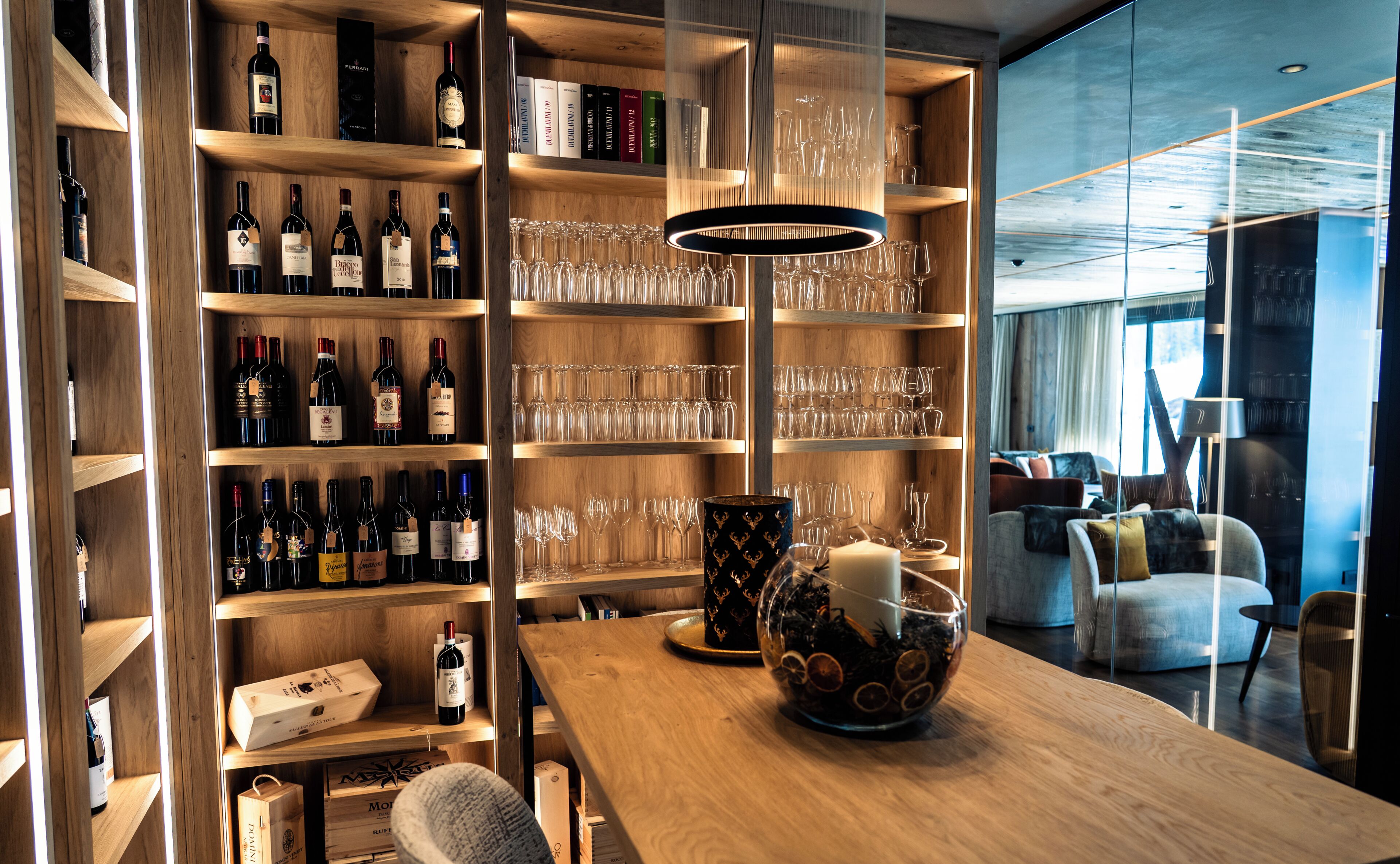 A well-organized wine cellar with shelves of wine bottles and glasses, a wooden table with a decorative bowl, and a modern interior design.