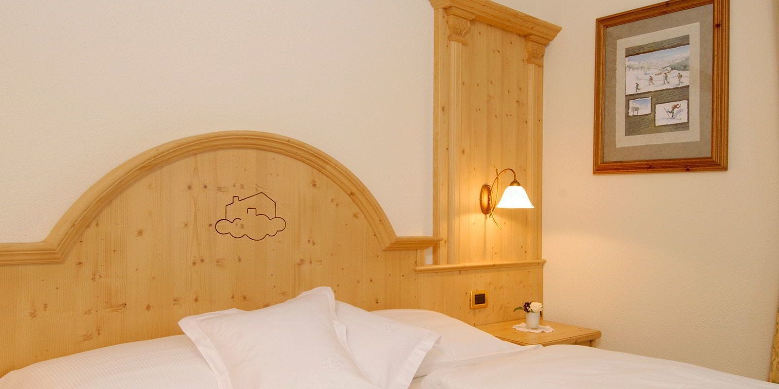Habitación de hotel con cabecera de madera, lámpara de noche, un cuadro enmarcado en la pared y una cama bien hecha.
