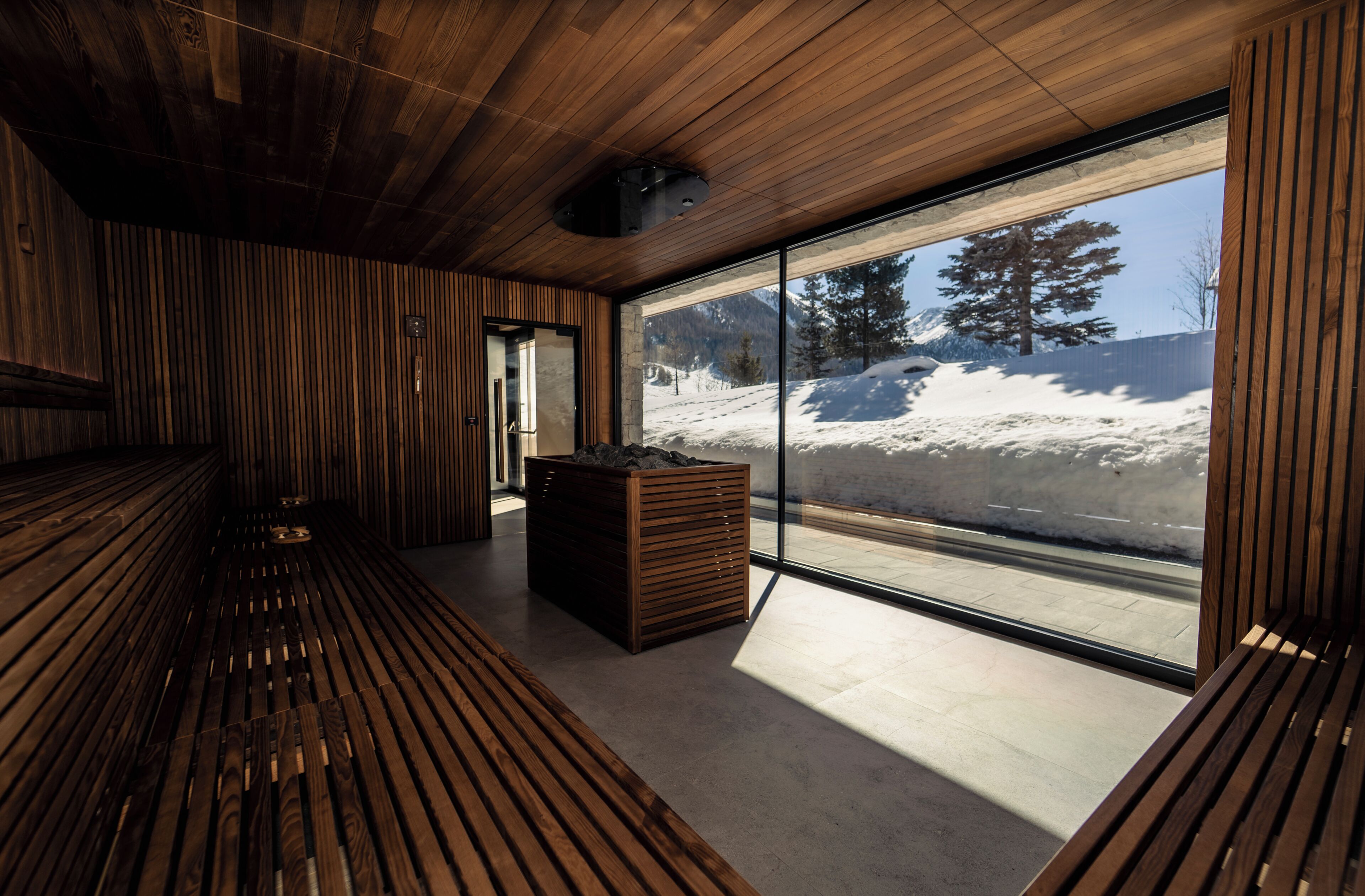 Un intérieur moderne avec un lambris en bois, un banc et une grande fenêtre donnant sur un paysage enneigé.