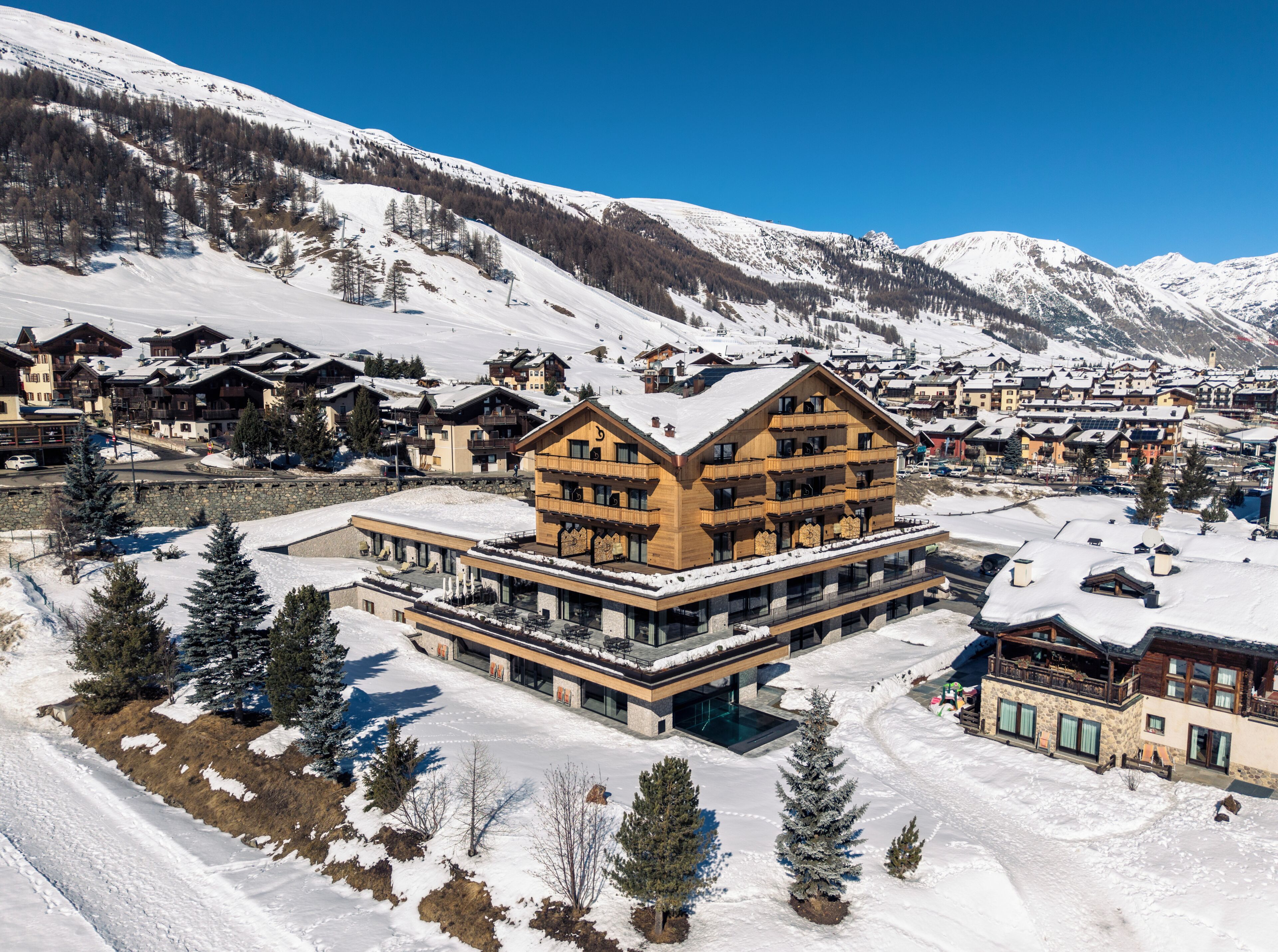 A multi-story wooden building with balconies, surrounded by snow-covered mountains and a ski resort.