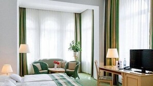 Een hotelkamer met een bed, een bureau, een stoel, een televisie en een plant.