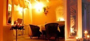 A warmly lit hallway with a dining area featuring two chairs and a table, a vase of flowers, and a wall-mounted light fixture.