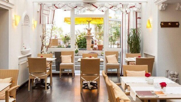 Een restaurant met rieten meubels, witte muren en uitzicht op de straat.