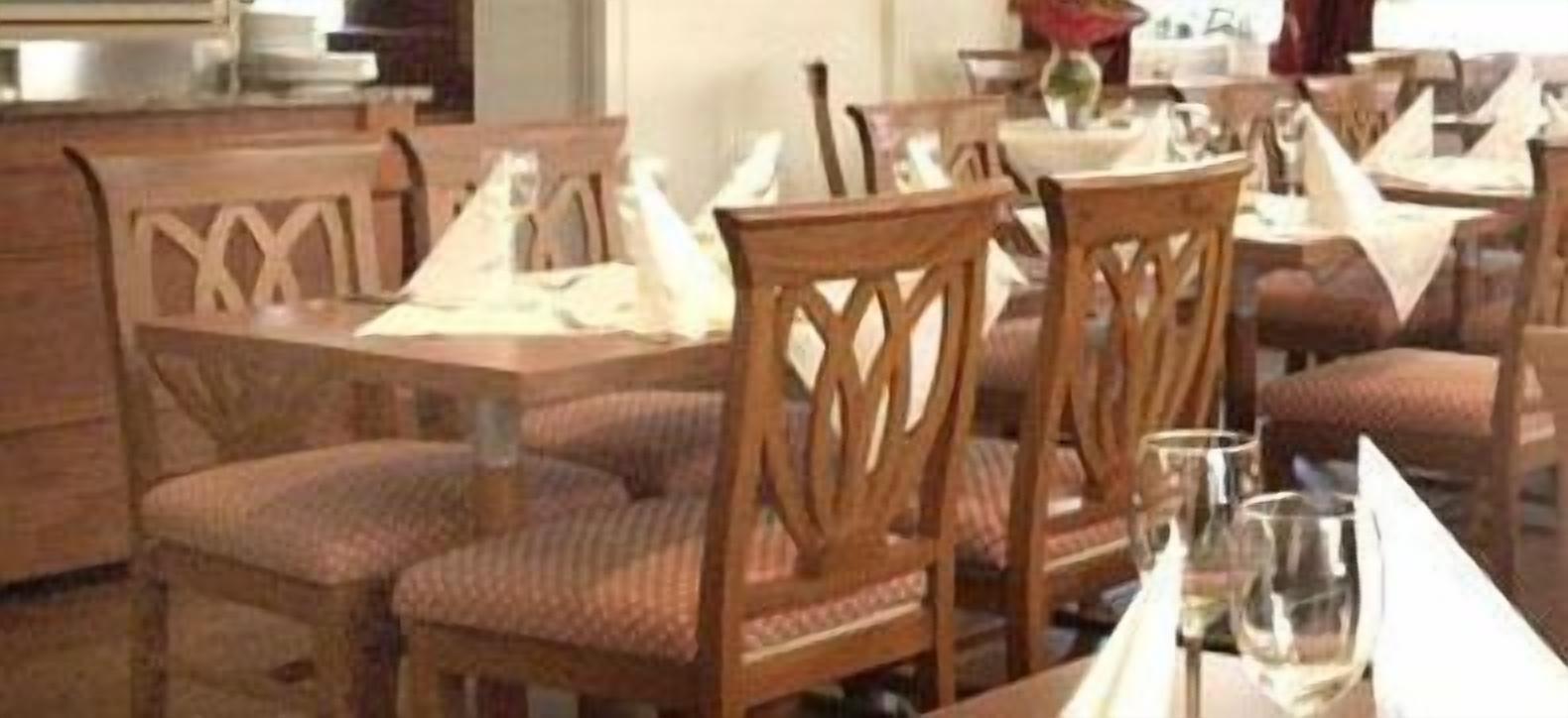 A restaurant with wooden chairs and tables, some with white tablecloths.