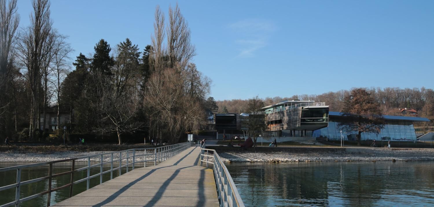 Eine Brücke über einem Fluss, am gegenüberliegenden Ufer ein modernes Gebäude.