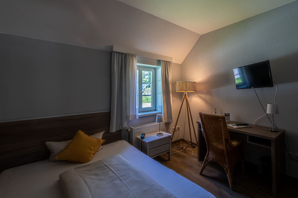 Habitación de hotel con cama, escritorio, silla, televisor y ventana con cortinas.