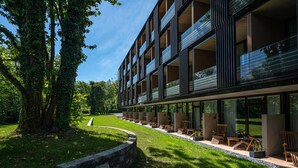 A modern building with a glass facade, outdoor seating area with chairs, and a well-maintained lawn. - Waldhaus Jakob (Konstanz)