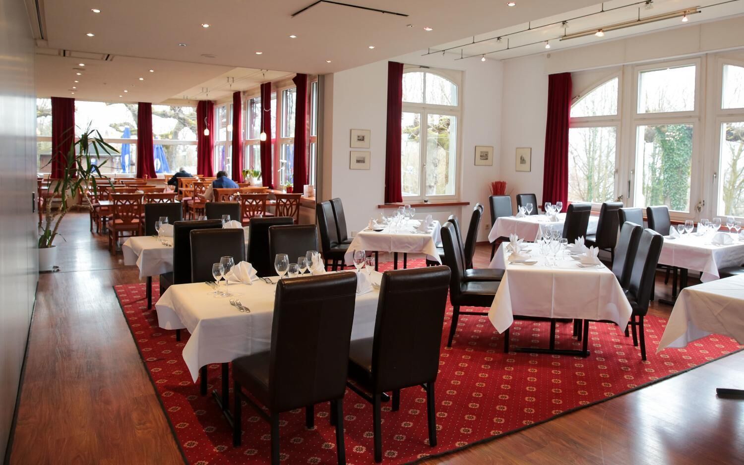 A restaurant with multiple tables set for dining, featuring a red carpet and white tablecloths.