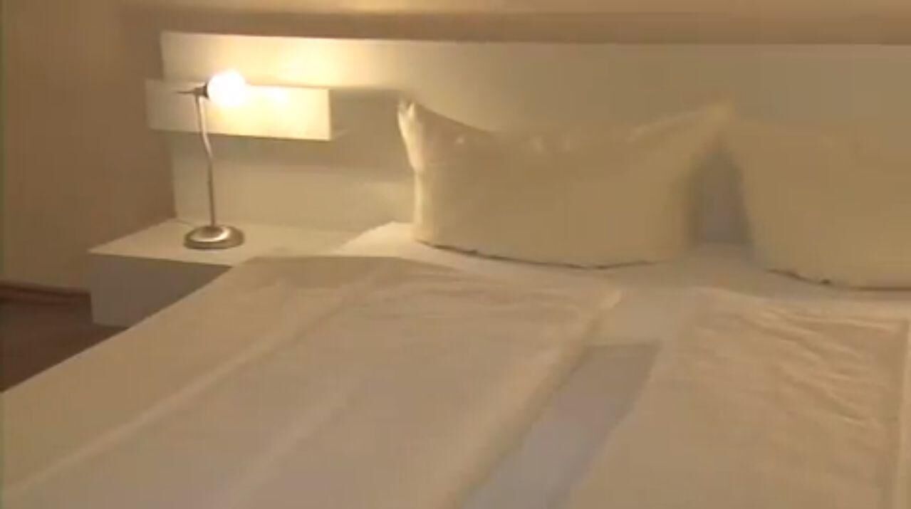 Ein ordentlich bezogenes Bett mit weißen Laken, einer Nachttischlampe und einem weißen Kopfteil.