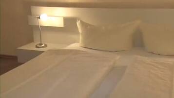 Ein ordentlich bezogenes Bett mit weißen Laken, einer Nachttischlampe und einem weißen Kopfteil.