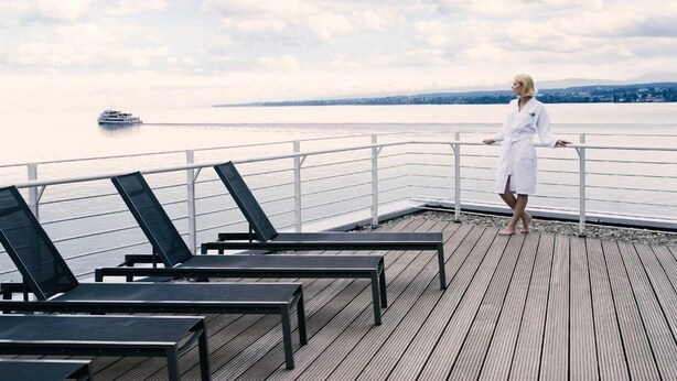 A deck with lounge chairs overlooking a calm body of water and a distant ship. - Waldhaus Jakob (Konstanz)