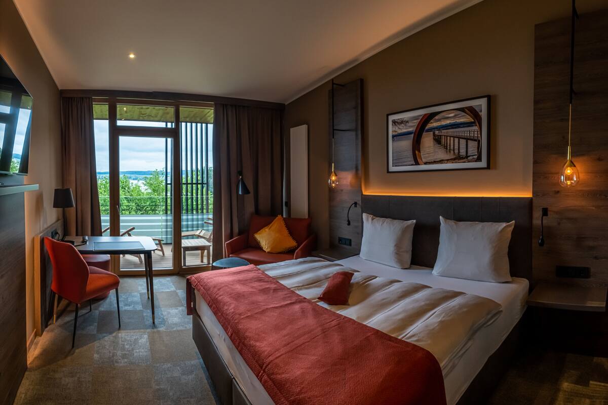 Habitación de hotel con una cama grande, un escritorio, una silla y un balcón con vistas.